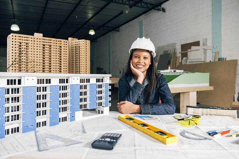 Ingénieure souriante en casque de chantier à côté d'une maquette de bâtiment